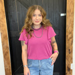 Woman wearing a pink top and blue jeans standing in front of a wooden door.