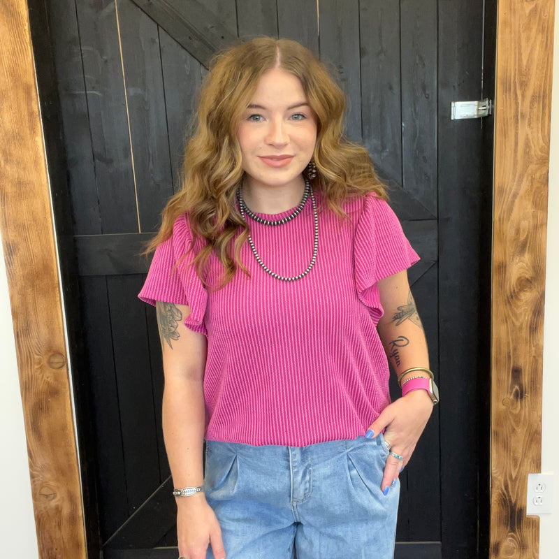 Woman wearing a pink top and blue jeans standing in front of a wooden door.