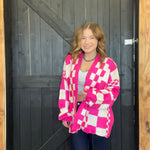 Woman wearing a pink and white checkered cardigan standing in front of a wooden door.