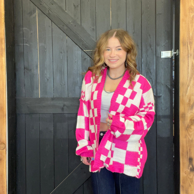 Woman wearing a pink and white checkered cardigan standing in front of a wooden door.