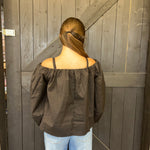 Person wearing a dark green off-shoulder top and light blue jeans standing against a wooden door.