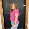 Woman in a pink top and blue jeans standing in front of a wooden door.