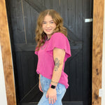 Woman in a pink top and blue jeans standing in front of a wooden door.