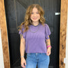 Person wearing a purple ribbed top and blue jeans standing in front of a wooden door.