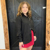 Woman wearing a black jacket over a red dress standing in front of a wooden door.