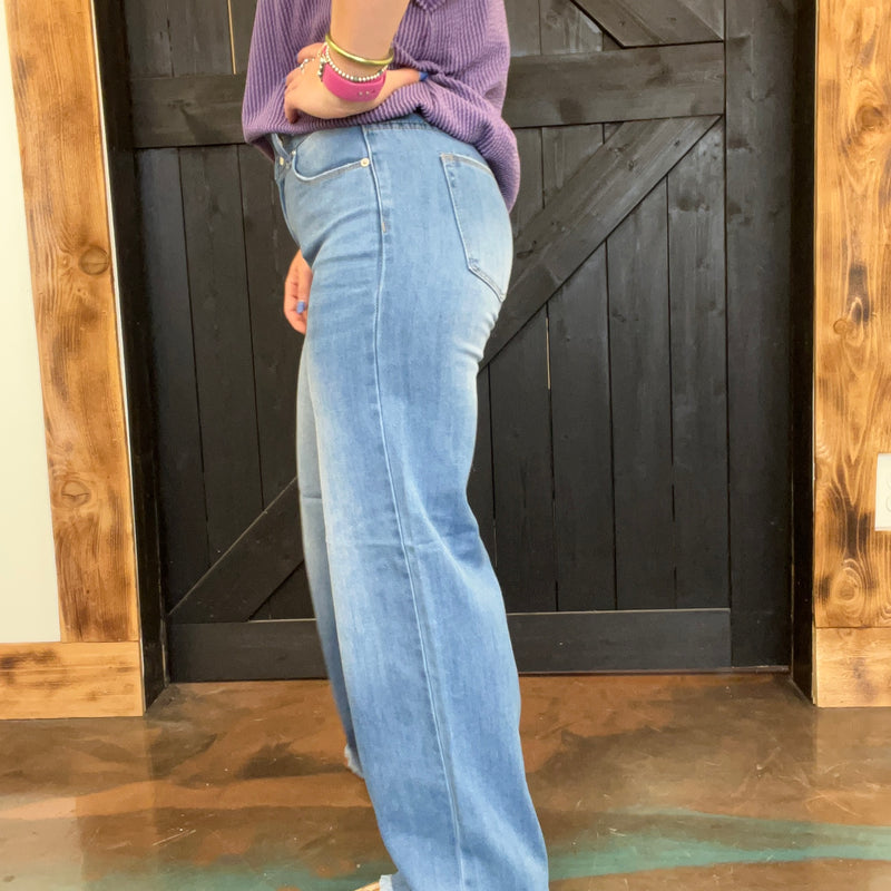 Person wearing light blue jeans and a purple sweater standing in front of a wooden door.