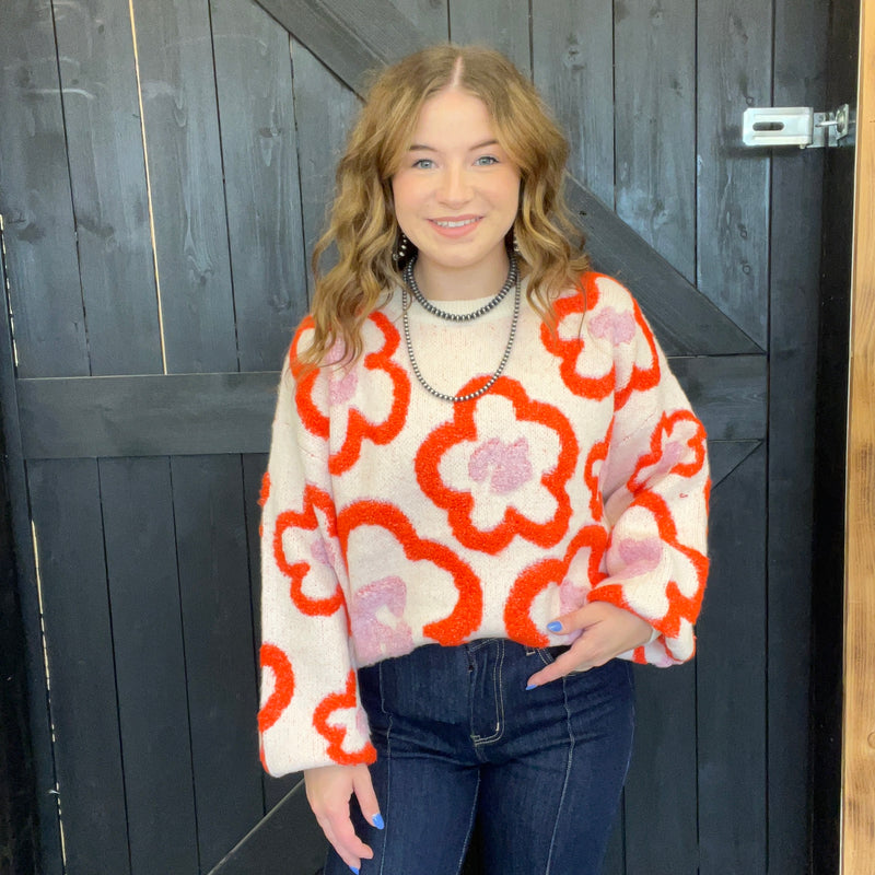 Person wearing a floral patterned sweater standing in front of a wooden door.