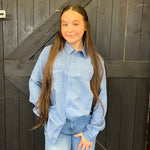 Person wearing a light blue shirt and jeans standing in front of a wooden door.