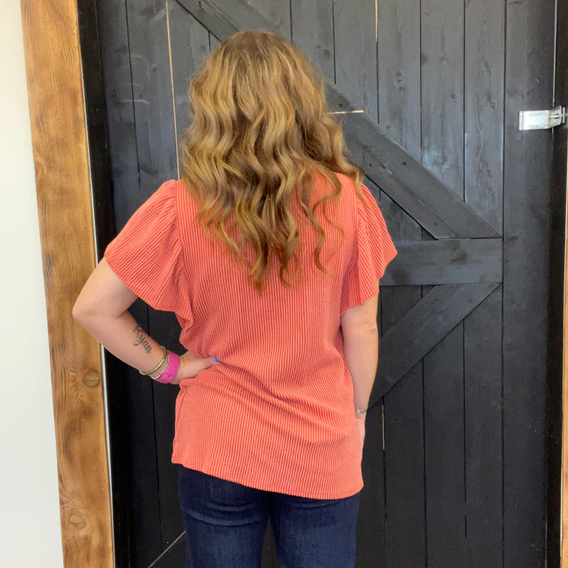 Person wearing an orange shirt standing in front of a wooden door.