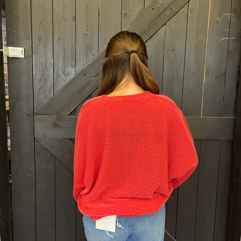 Person wearing a red sweater and blue jeans standing in front of a wooden door.