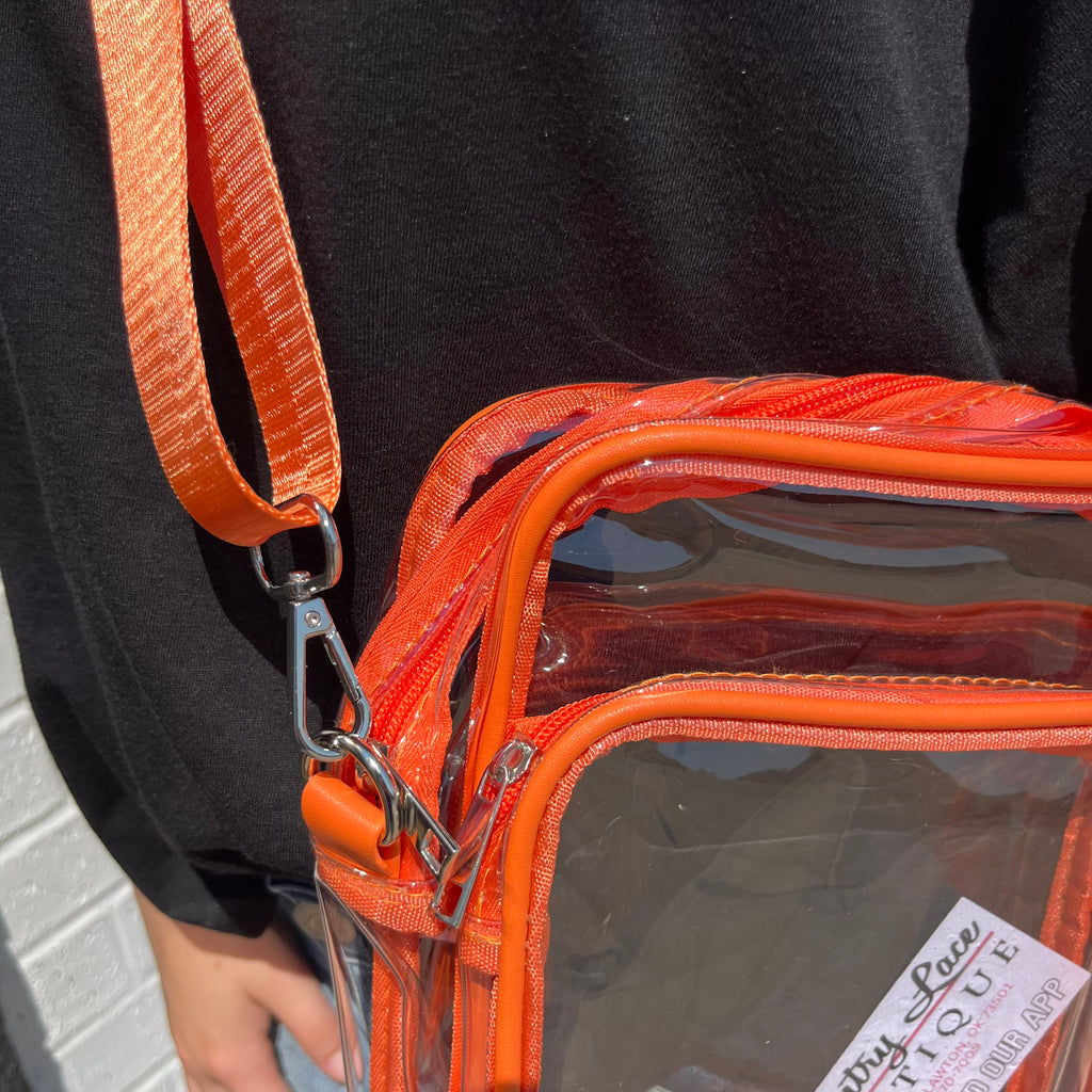 Orange transparent bag with a brown strap held by a person wearing a black shirt.