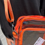 Orange transparent bag with a brown strap held by a person wearing a black shirt.
