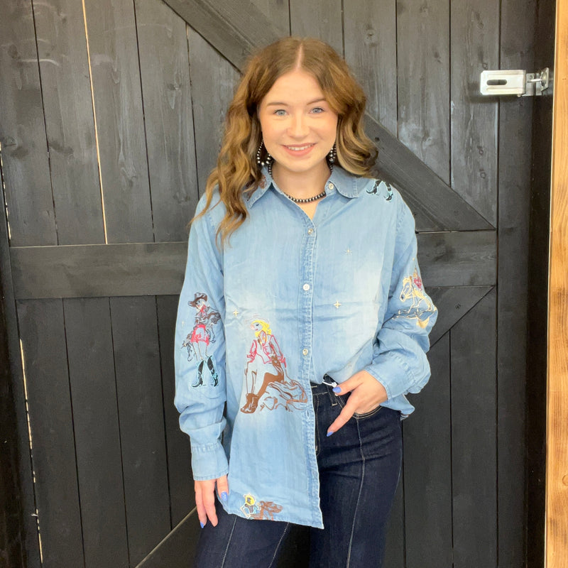 Woman wearing a light blue denim shirt with embroidered designs in front of a wooden door.