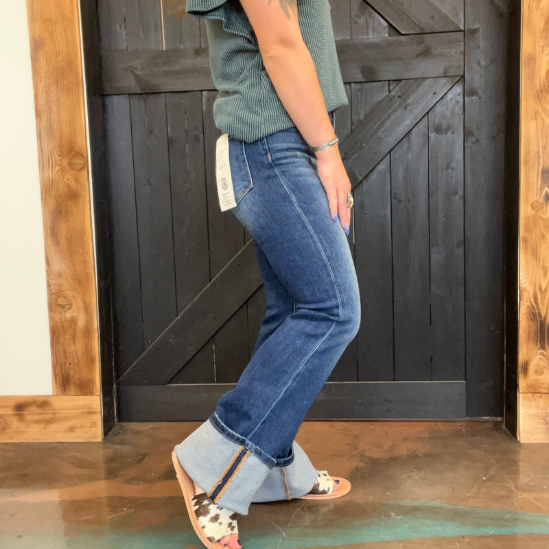 Person wearing blue jeans and sandals standing in front of a wooden door.