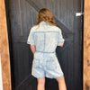 Person wearing a denim romper standing in front of a wooden door.