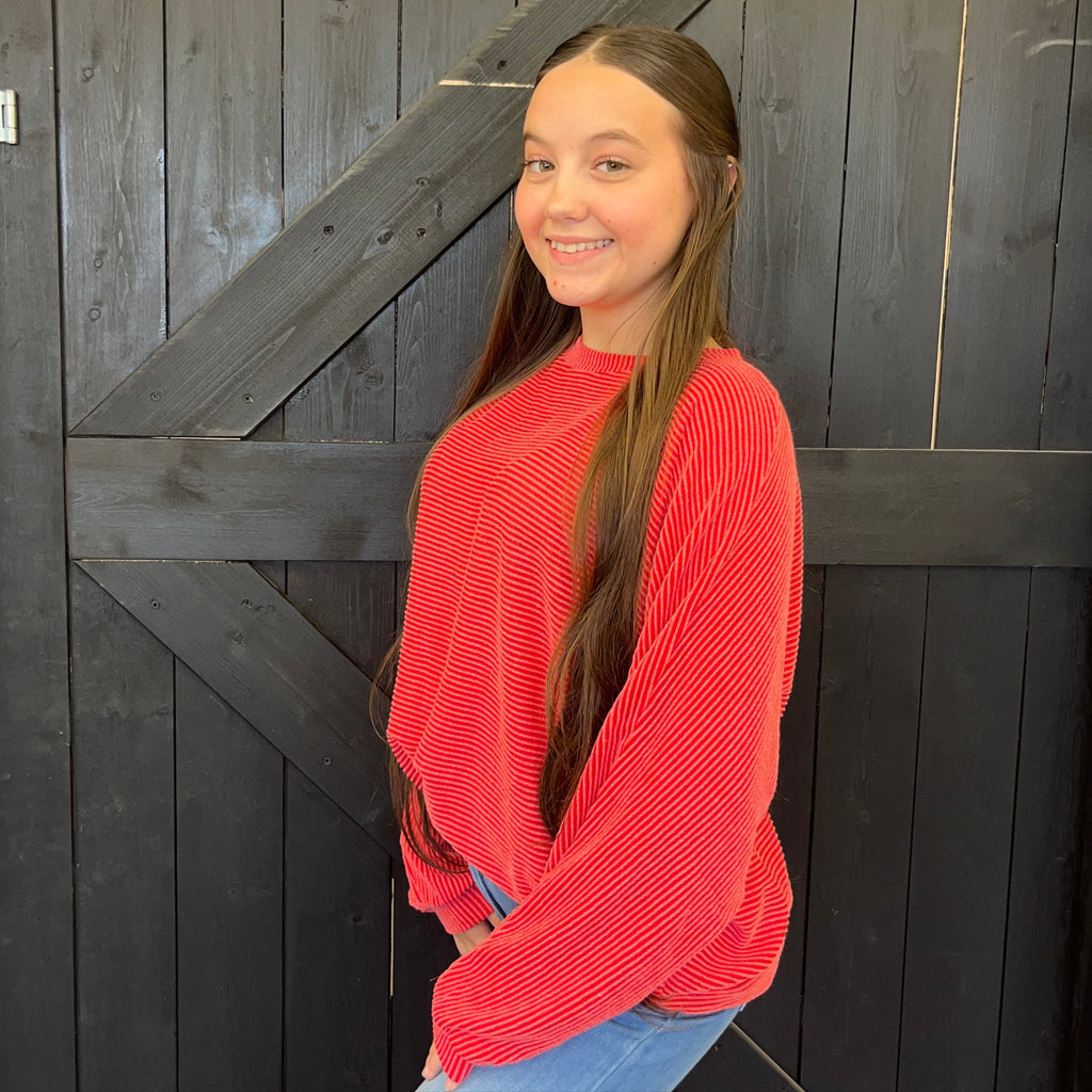 Young girl in a red sweater standing in front of a dark wooden door