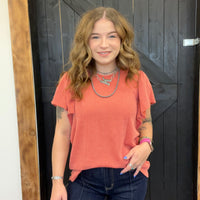 Woman wearing a coral top and dark jeans standing in front of a wooden door.