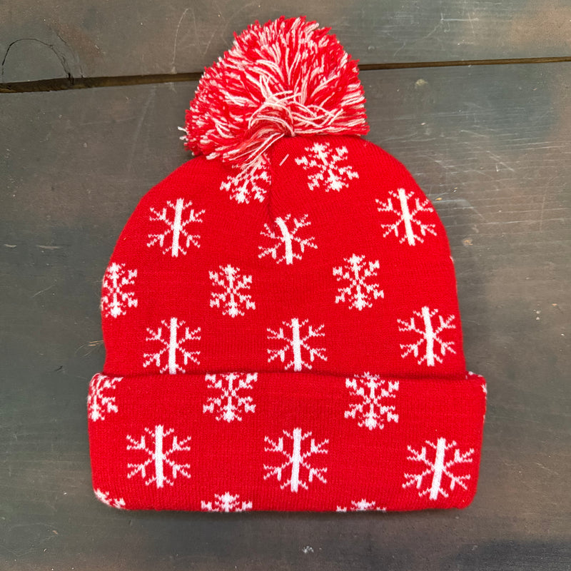 Red knit beanie with white snowflake pattern on a gray surface