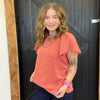 Woman wearing an orange top standing in front of a wooden door.