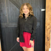 Woman wearing a black shirt and red shorts standing in front of a wooden door.