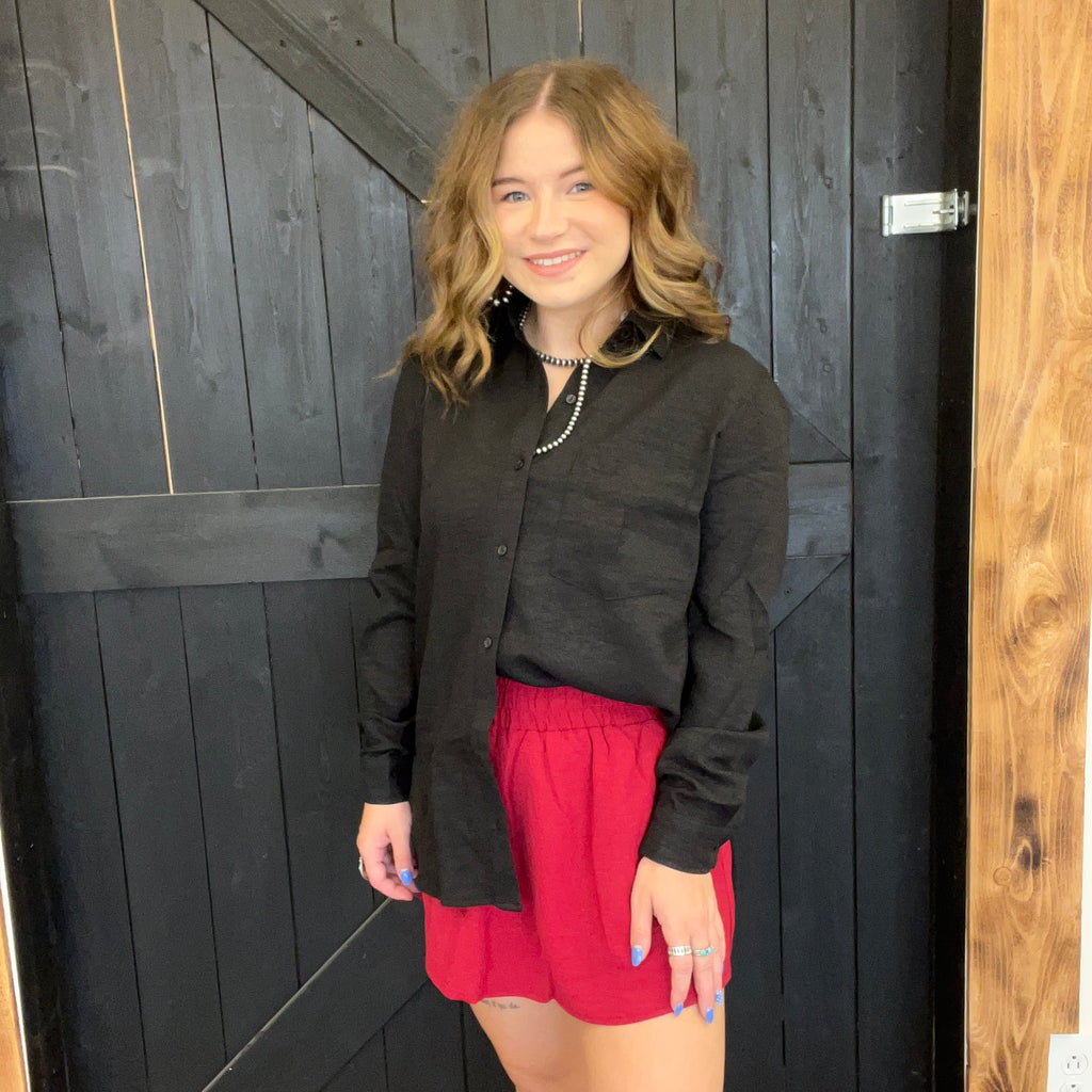Woman wearing a black shirt and red shorts standing in front of a wooden door.