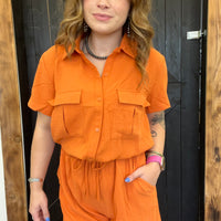 Person wearing an orange outfit standing against a wooden and black door background