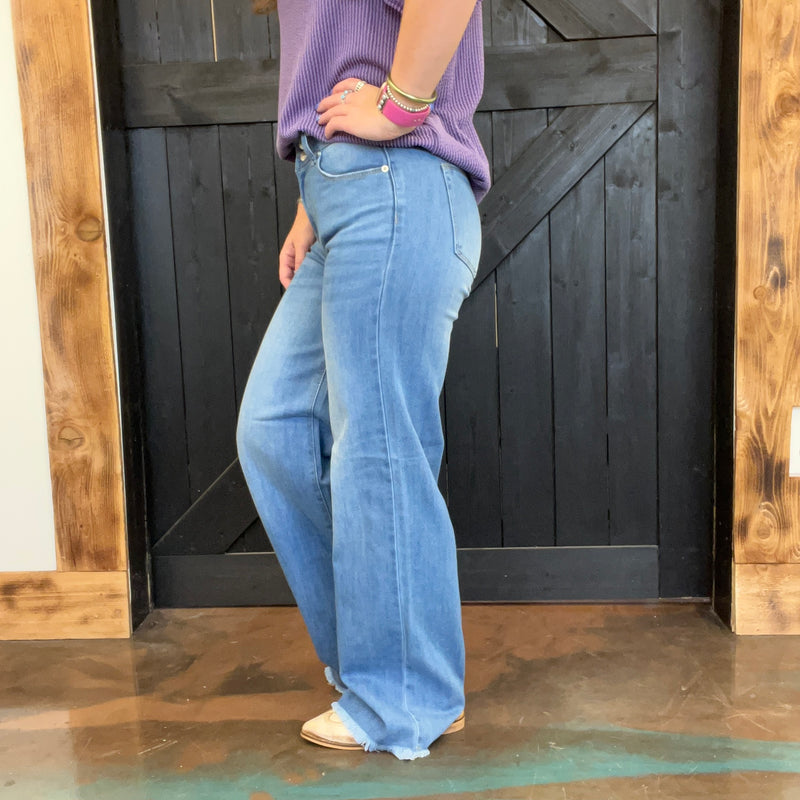 Person wearing blue jeans and a purple top standing in front of a wooden door.