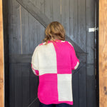  pink and white checkered sweater standing in front of a wooden door.
