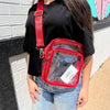 Person wearing a clear crossbody bag with red straps against a brick wall.