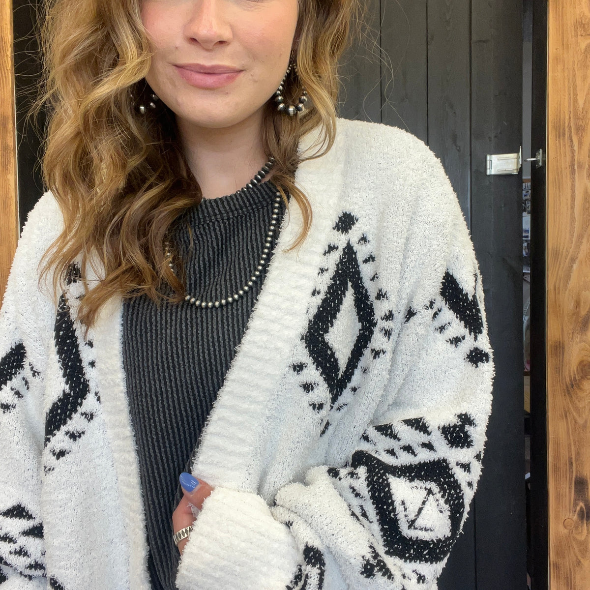 Woman wearing a white cardigan with black patterns, standing indoors.