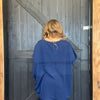 Person wearing a blue sweater standing in front of a wooden door.