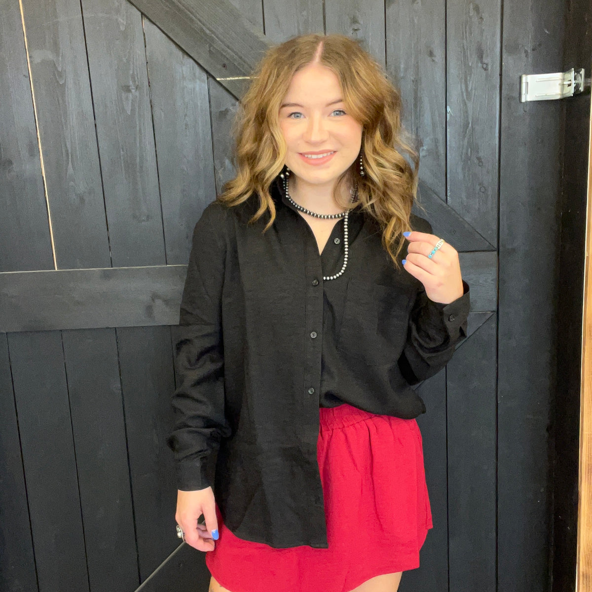 Woman wearing a black shirt and red skirt standing against a dark wooden wall.