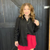 Woman wearing a black shirt and red skirt standing against a dark wooden wall.