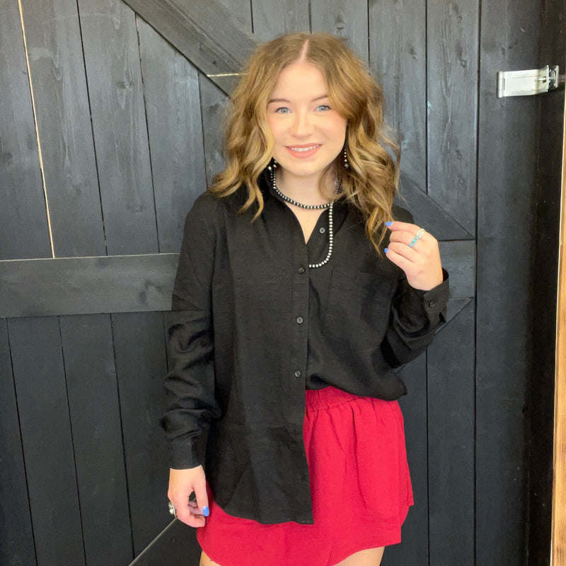 Woman wearing a black shirt and red skirt standing against a dark wooden wall.