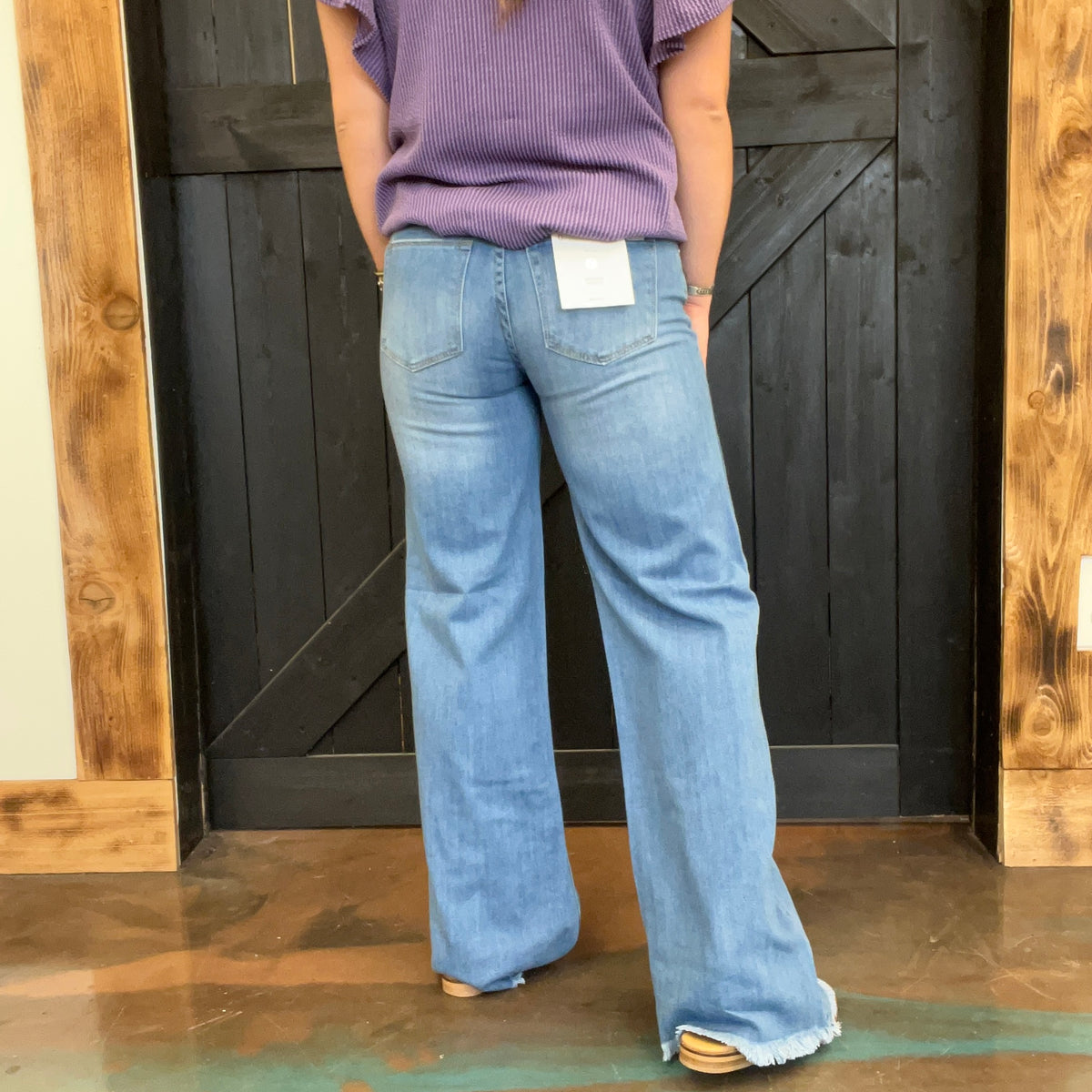 Person wearing blue jeans with a visible brand tag, standing in front of a wooden door.