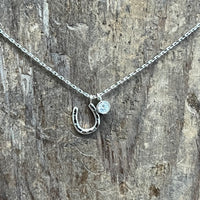 Silver necklace with a horseshoe and gemstone pendant on a wooden background