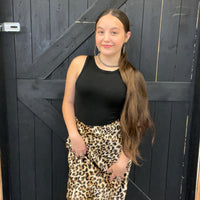 Woman wearing a black top and leopard print skirt standing in front of a dark wooden door.