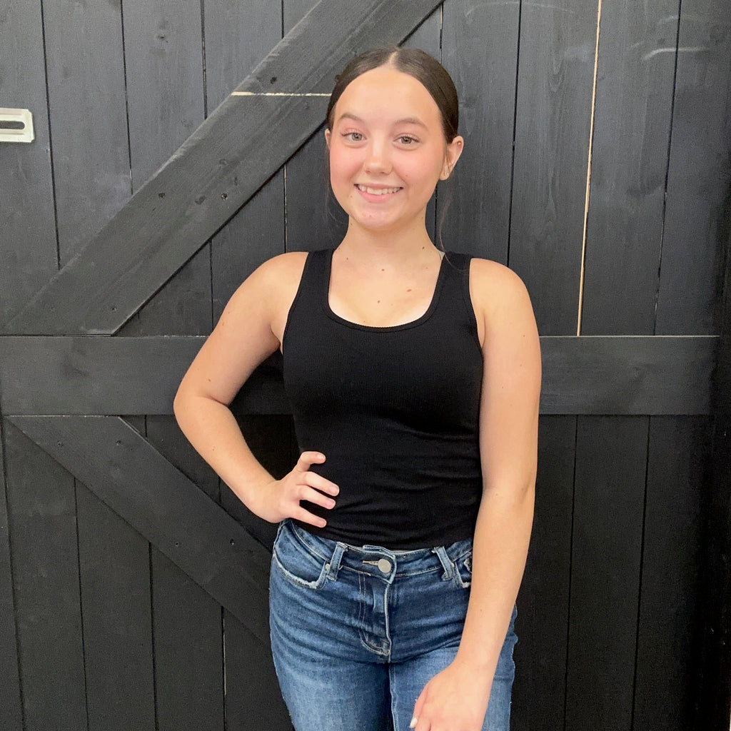  black tank top and blue jeans standing against a dark wooden background