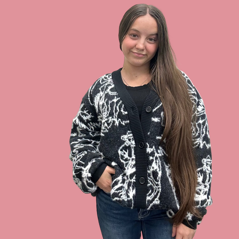 Person wearing a black and white patterned cardigan against a plain background