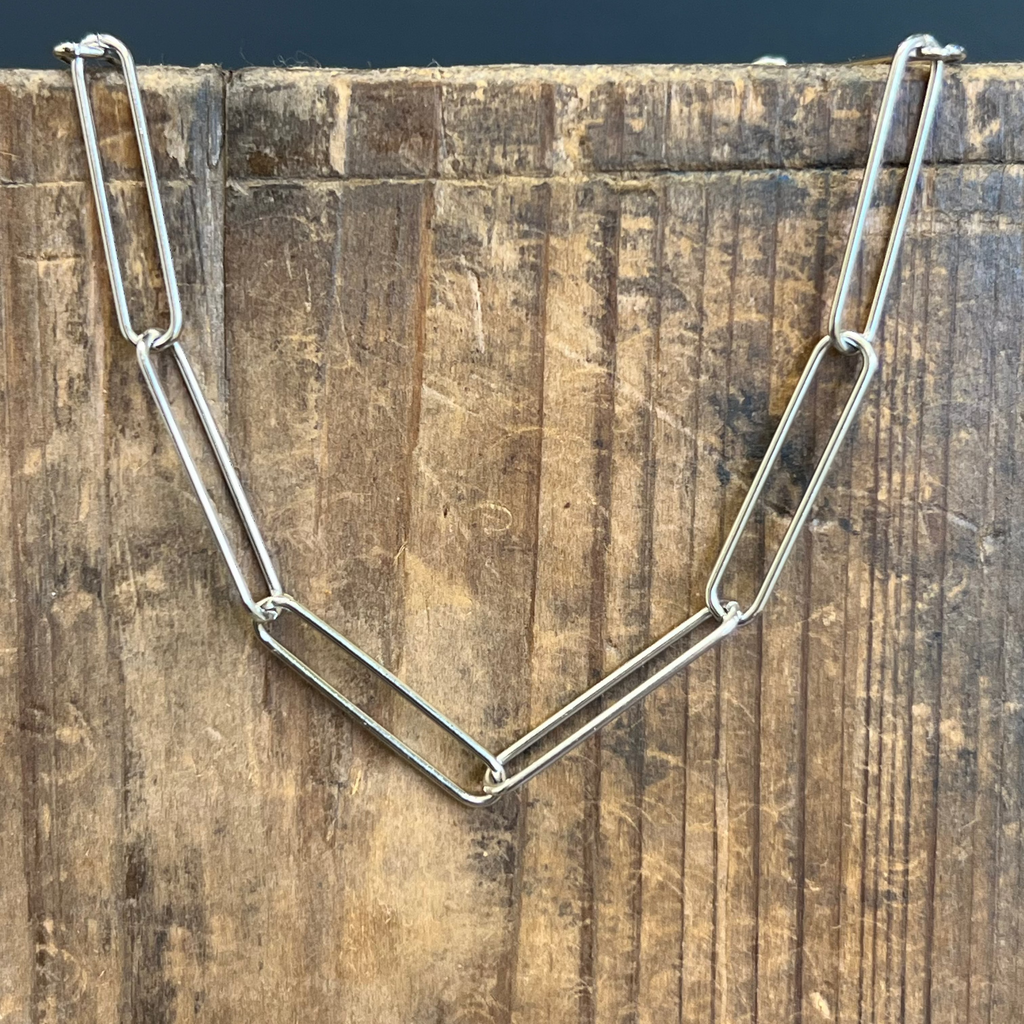 Silver chain necklace on a wooden surface with a dark background