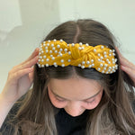 Person wearing a yellow headband with pearls on a plain background