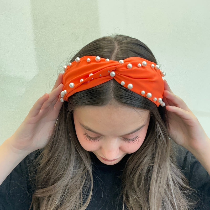 Person wearing an orange headband with pearls on a plain background