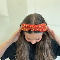 Person wearing a red headband with gold embellishments on a white background