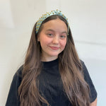 Young girl wearing a light blue headband with gold studs against a white background
