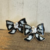 Bow-shaped Halloween-themed pins with ghosts and 'BOO!' text on a wooden surface.