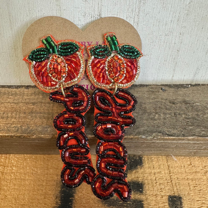 Decorative earrings with peach design and 'Happy' text on a wooden surface
