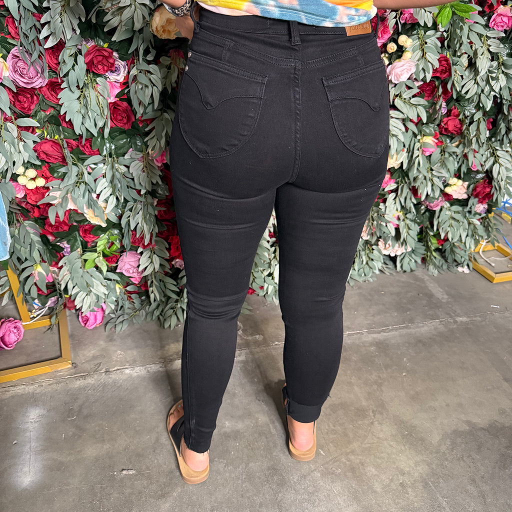 Person wearing black jeans standing in front of a floral wall.