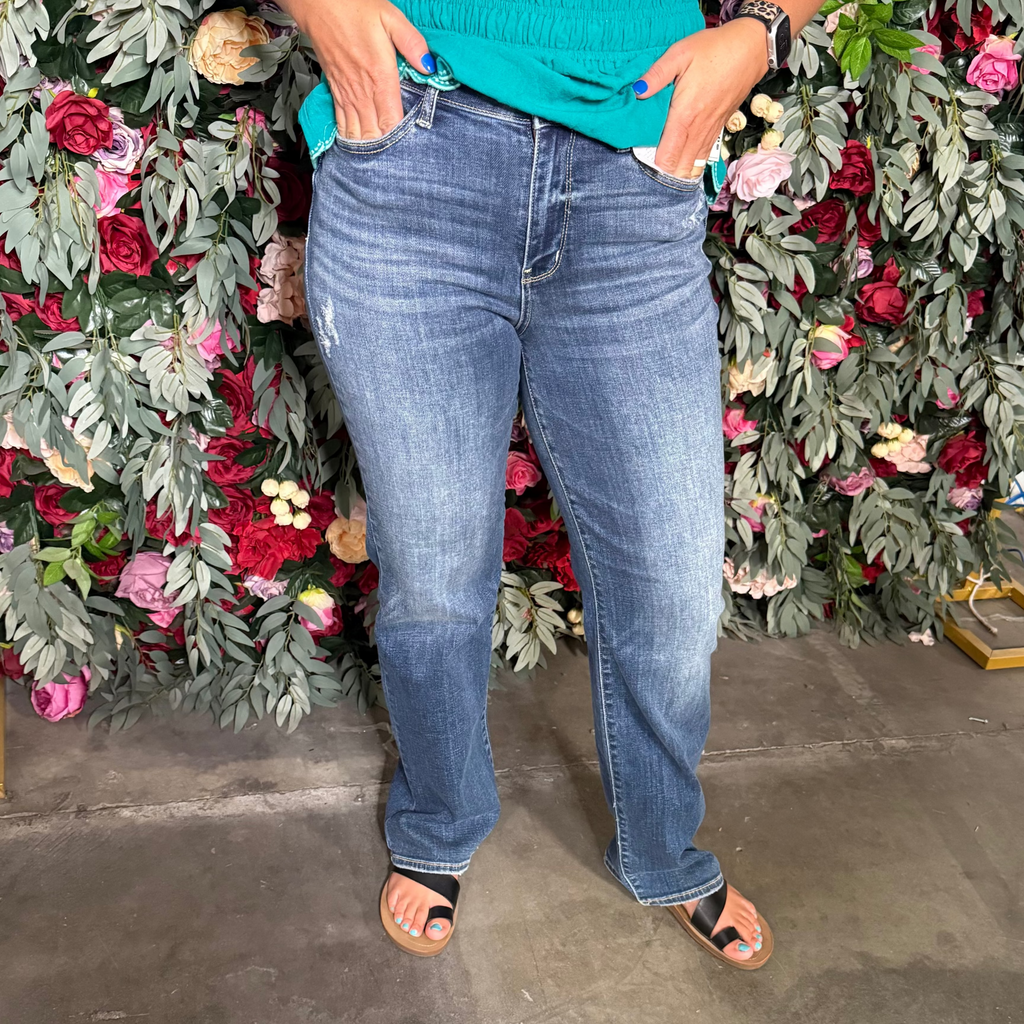 Person wearing blue jeans standing in front of a floral wall.