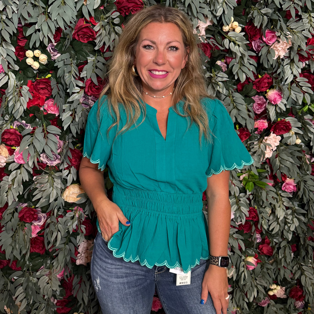 Woman in a teal top standing in front of a floral wall