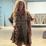 Woman wearing a leopard print dress in an indoor setting with a blue curtain and wooden beams.